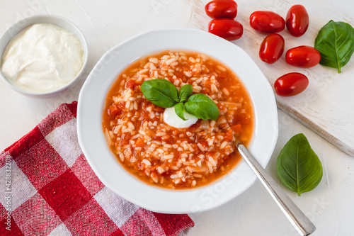 Fotografie Tomato soup with rice decorated by cream and basil leaf.