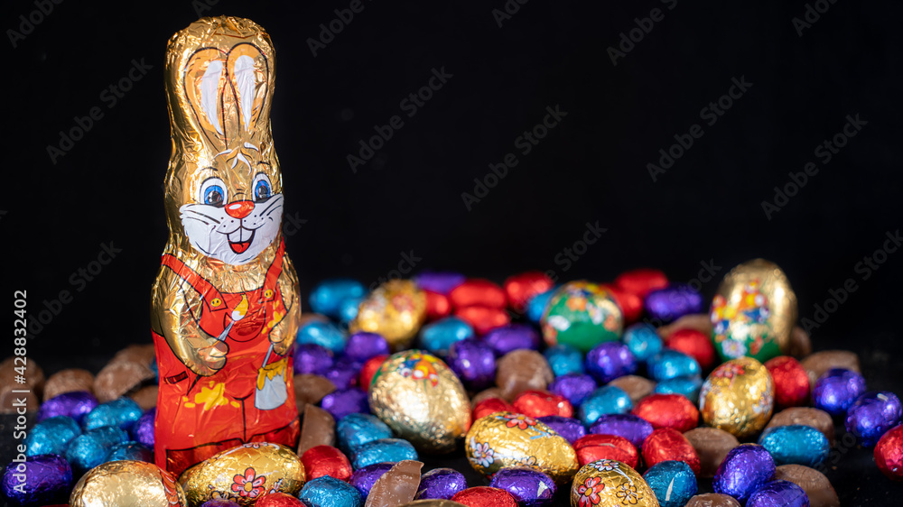 Easter bunny surrounded by multicolored eggs and chocolates, on black background