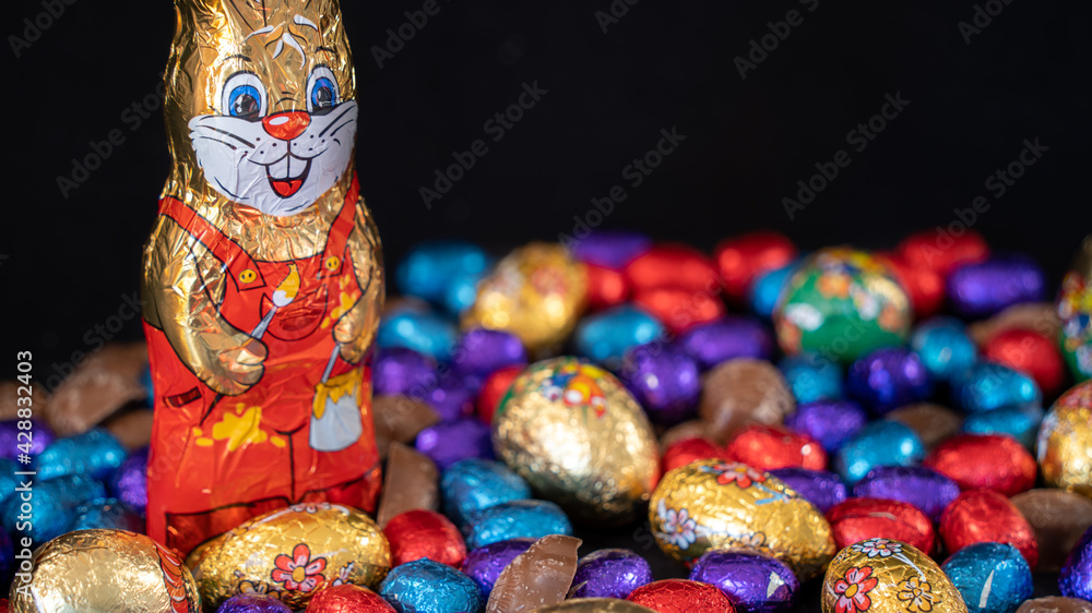 Easter bunny surrounded by multicolored eggs and chocolates, on black background