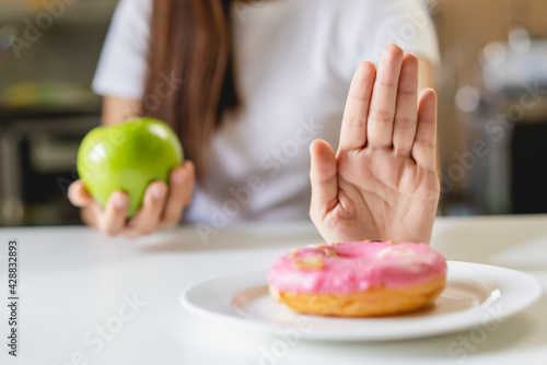 Woman on dieting for good health concept. Close up female using hand push out her favourite donut and choose green apple and vegetables for good health.