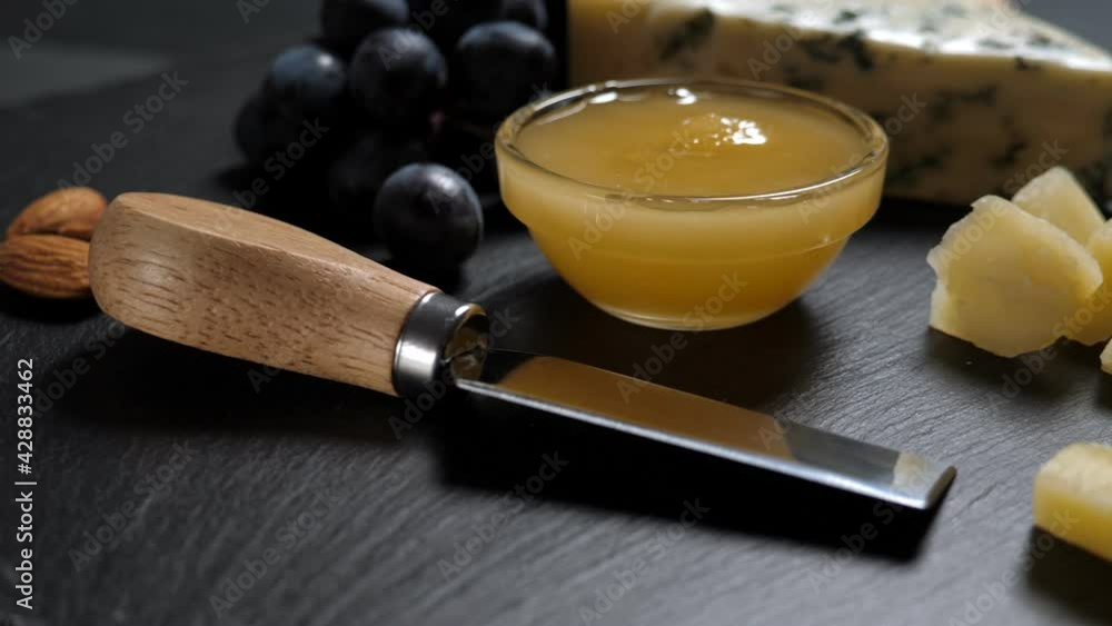 Sliced cheese, nuts, grape, honey and knife on shale platter. Rotating on slate background Sliced cheese, nuts, grape, honey and knife on shale platter. Rotating on slate background