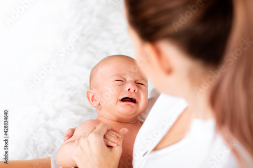 Mother with tail in white shirt holding crying newborn baby. Copy space.