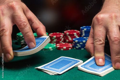 Close-up hands of a person-dealer or croupier shuffling poker cards in a poker club on background of a table, chips. Poker game or gaming business concept