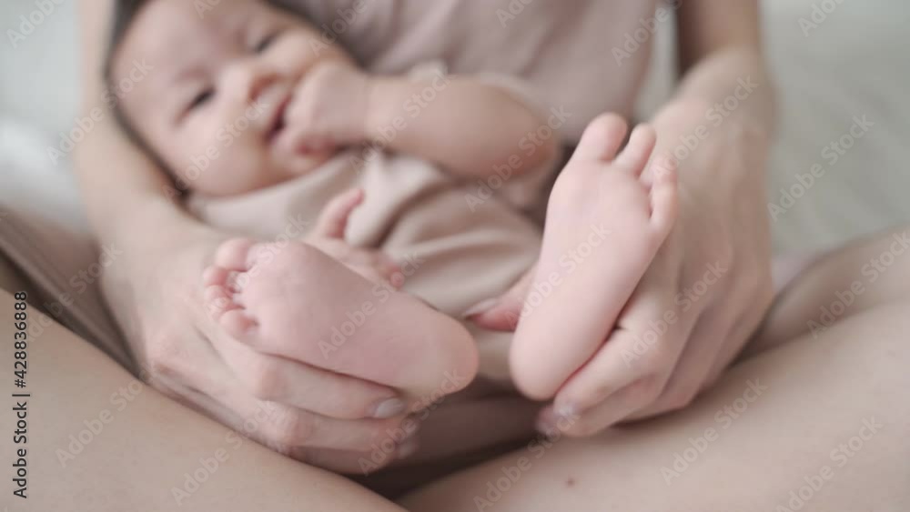 asian woman mother parent touching baby infant feet with love and care on soft bed. close up female hand holding baby foot. love protection concept. asian woman mother parent touching baby infant feet with love and care on soft bed. close up female hand holding baby foot. love protection concept.
