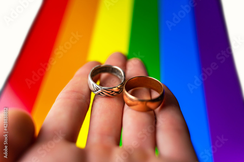 gay wedding proposal. hand holds two wedding rings on lgbt flag background. same-sex marriage, homosexuality and legalized relationship of two lgbt people.. photo