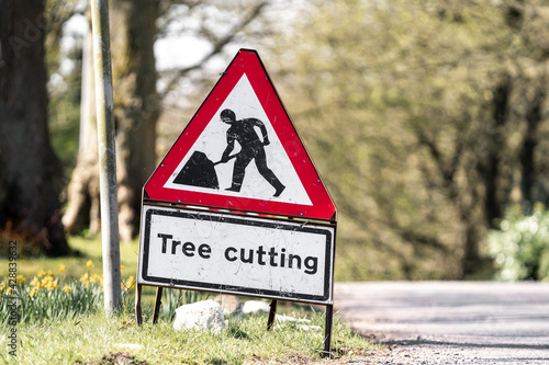 Red and white tree cutting warning sign standing at side of road with road works worker symbol.  Traffic sign alerting drivers of danger.