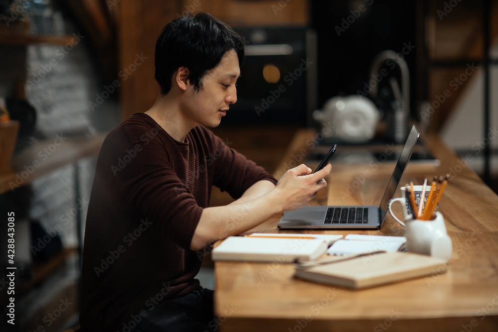 Fototapeta premium Asian man using smartphone while working at home