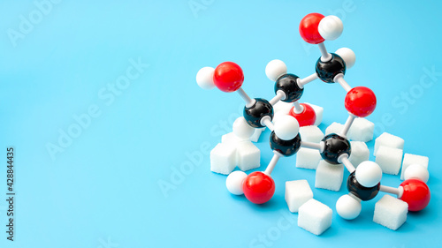 Simple sugars, diabetes awareness and chemical structure of carbohydrates concept with plastic model of the glucose molecule and sugar cubes isolated on blue background with copy space photo