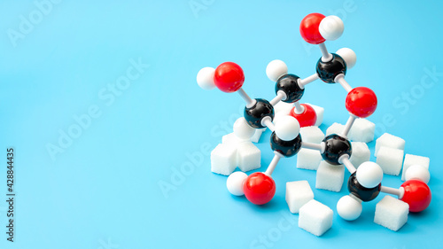 Obraz na płótnie Simple sugars, diabetes awareness and chemical structure of carbohydrates concept with plastic model of the glucose molecule and sugar cubes isolated on blue background with copy space w salonie