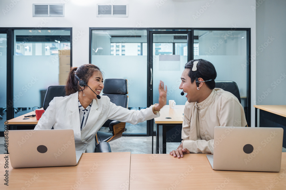 Friendly operator asian colleague with headset and laptop talking gossip between working in call centre Friendly operator asian colleague with headset and laptop talking gossip between working in call centre