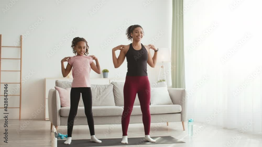 Happy african american mother and daughter warming up shoulders, preparing for domestic workout at home Happy african american mother and daughter warming up shoulders, preparing for domestic workout at home