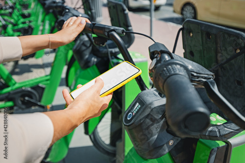 Woman uses an app in her smartphone to rent a shared electric bike for a trip around the city. Solving the problem of transport in the metropolis