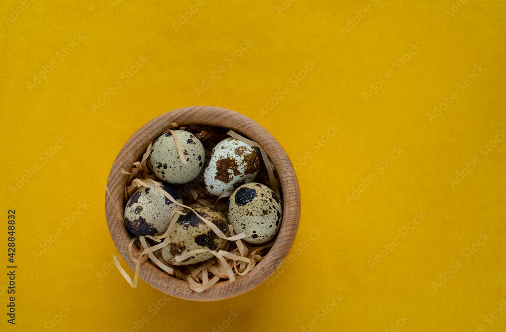 Quail eggs in the wooden basket on the yellow background Quail eggs in the wooden basket on the yellow background