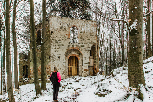 Fototapeta Naklejka Na Ścianę i Meble -  Hiking girl enjoying view of ruins of abandoned Chapel of Saint Mary Magdalene on the hill of Maly Blanik,central Bohemia,Czech Republic.Pilgrimage place with great spruce growing within chapel walls