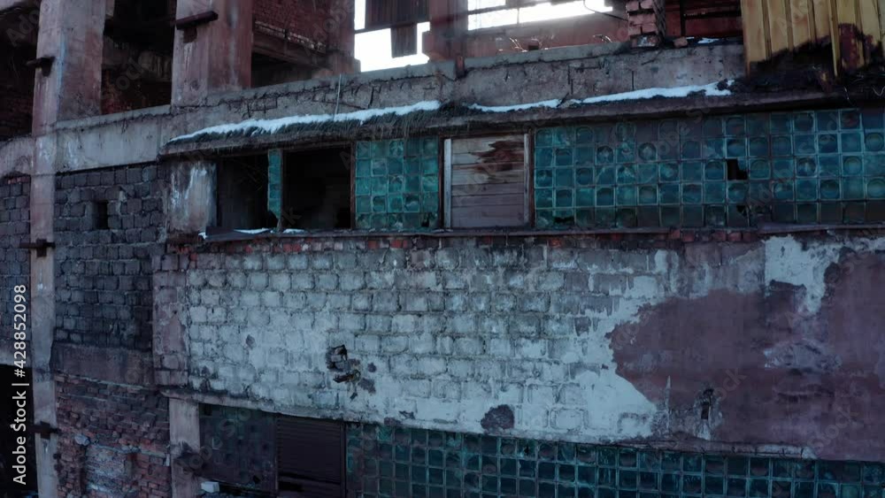 Sun shines through floors of vacant deteriorating industrial building, drone rise up shot