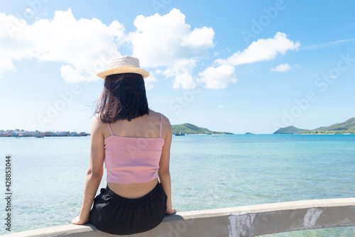 Back of asian woman tan skin wearing pink tank top and straw hat sitting on mortar and holding hand on mortar. Summer travel. Relaxing, Holiday and tropical Alone travel concept.