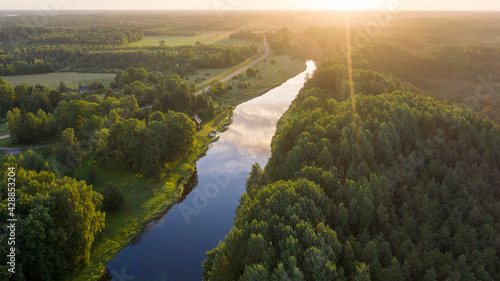 Aerial view along natural river toward sunny morning horizon and wilderness of the national park on the right side and rural landscape on the left