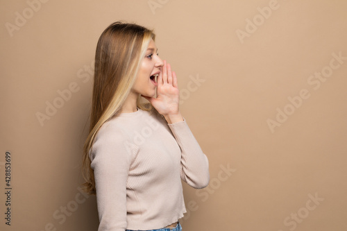 Excited beautiful woman looking and screaming aside isolated over beige background