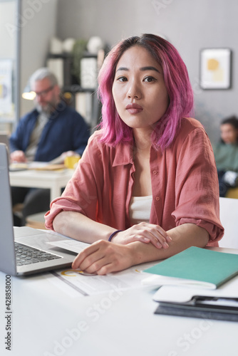 Portrait of Asian student looking at camera while sitting at the table and working on laptop