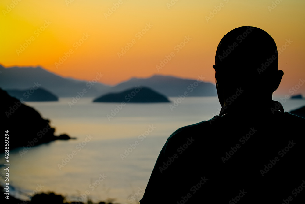 Fototapeta premium Uma pessoa de costas de sillhueta para o mar para ver o lindo nascer do sol sobre as rochas na cor amareladas e pretas.