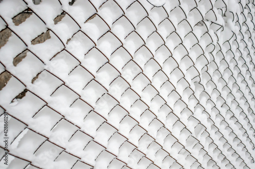 Metal fence made of mesh netting covered with snow in nature as a background.