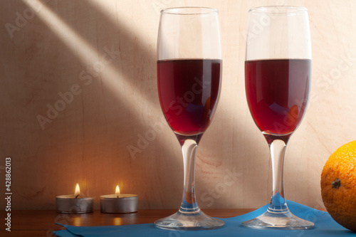 Still life with two glasses of wine on a blue napkin, an orange and two burning candles.