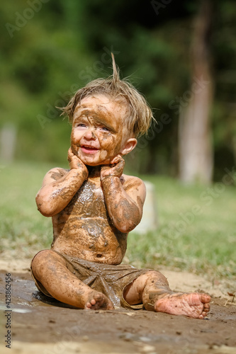 Criança brincando na lama linda com sorriso perfeito.