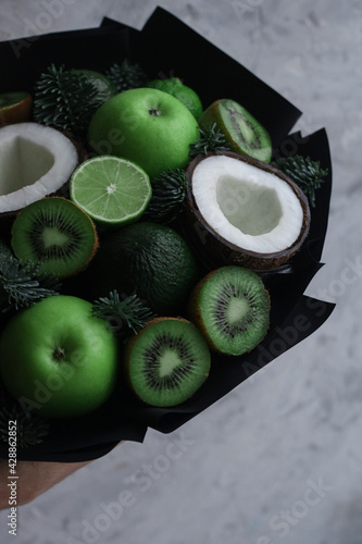 fruit bouquet of green fruits and coconut in black packaging on concrete background