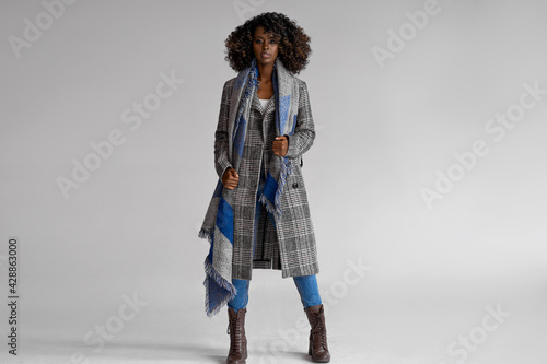 Female black model wear grey plaid coat with scarf with a trendy afro hairstyle isoalted on gray