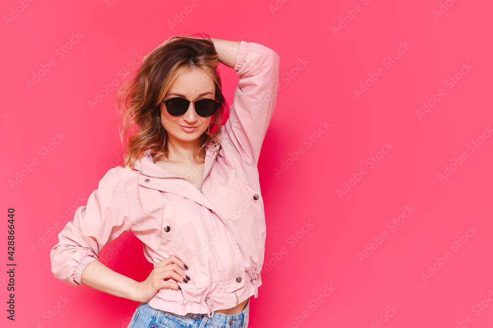 A young pretty caucasian confident brown-haired woman in a casual stylish jacket and black sunglasses poses with her hand on a head on a bright color pink background. Beauty, fashion. Copy space A young pretty caucasian confident brown-haired woman in a casual stylish jacket and black sunglasses poses with her hand on a head on a bright color pink background. Beauty, fashion. Copy space