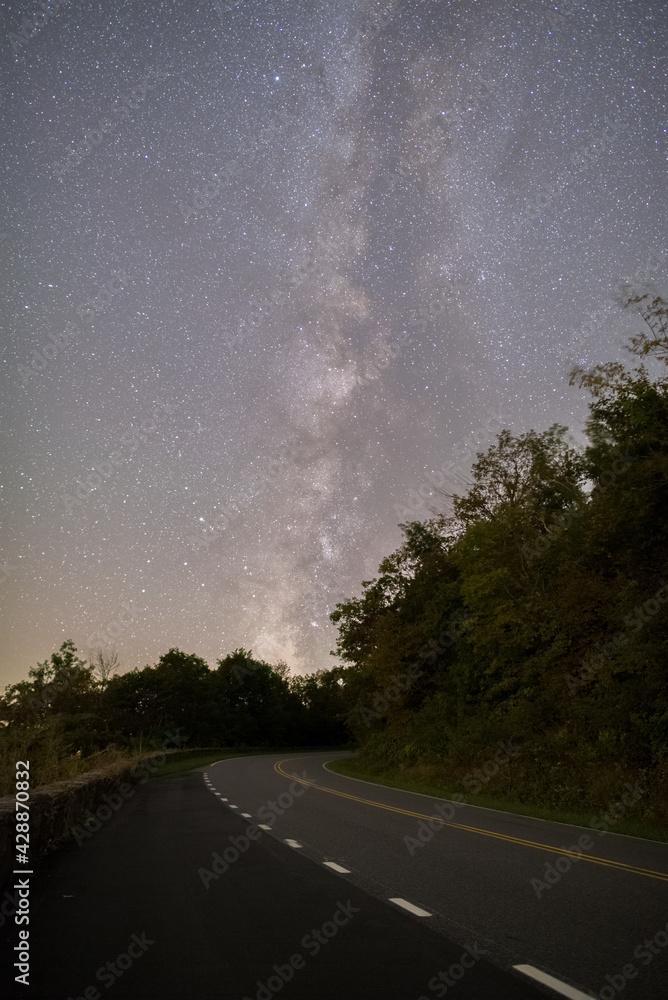 Naklejka premium The Milky Way galaxy rising over a curving mountain road