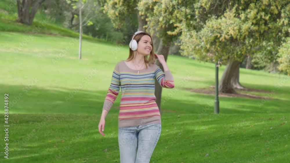 People in nature, lifestyle and joy video concept. Slow motion of happy young woman in headphones during morning walk having good time and relaxing in green city park. RED Helium Weapon footage shot People in nature, lifestyle and joy video concept. Slow motion of happy young woman in headphones during morning walk having good time and relaxing in green city park. RED Helium Weapon footage shot