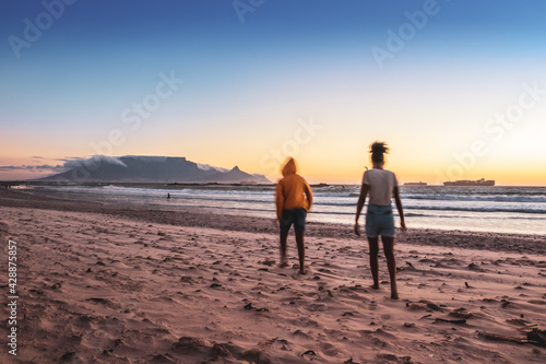 Two African women walking on the beach at sunset, with Table Mountain and Cape Town in the background, Milnerton Beach, Cape Town, South Africa