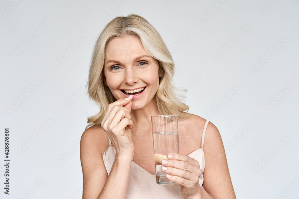 © insta_photos - Happy middle aged 50s woman holding pill and glass of water taking dietary supplements. Portrait of smiling adult attractive woman taking care of health in menopause, isolated on white. © insta_photos - Happy middle aged 50s woman holding pill and glass of water taking dietary supplements. Portrait of smiling adult attractive woman taking care of health in menopause, isolated on white.