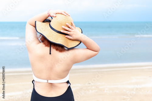 A young women standing with her back in a swimming suit and a sun hat on the beach.Beach vacation.Copy space. photo