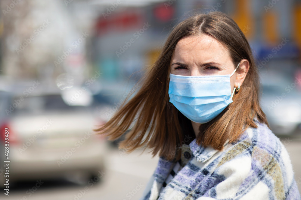 A young woman in a medical mask stands in a parking lot near a grocery store. A woman is protecting herself from the coronavirus. Shopping during quarantine A young woman in a medical mask stands in a parking lot near a grocery store. A woman is protecting herself from the coronavirus. Shopping during quarantine