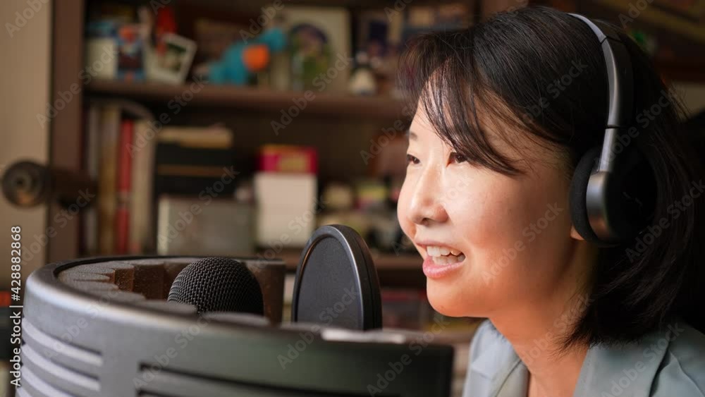 Close up shot of Asian young woman wearing headphone talking for voice over to record with condenser microphone with noise absorbing barrier, Podcaster or blogger recording voice from home studio. Close up shot of Asian young woman wearing headphone talking for voice over to record with condenser microphone with noise absorbing barrier, Podcaster or blogger recording voice from home studio.