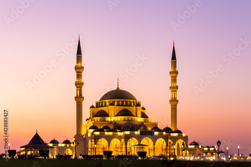 New Sharjah Mosque, the largest mosque in the Emirate of Sharjah, the United Arab Emirates, with pink sky sunset and facade illuminations in the evening.