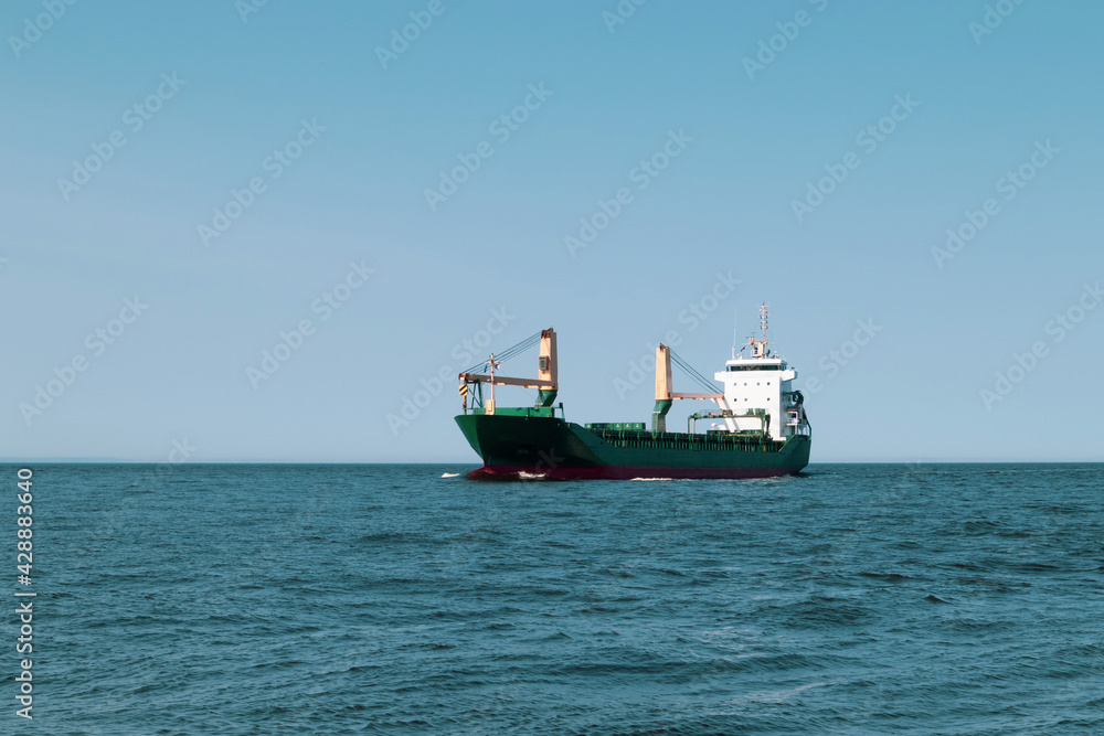 A green cargo ship is sailing at sea
