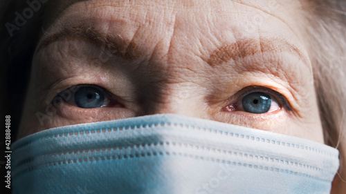 Close up on the blue eyes of an old gray haired woman with face mask. Vulnerable aged person and covid19. High quality photo © CameraCraft
