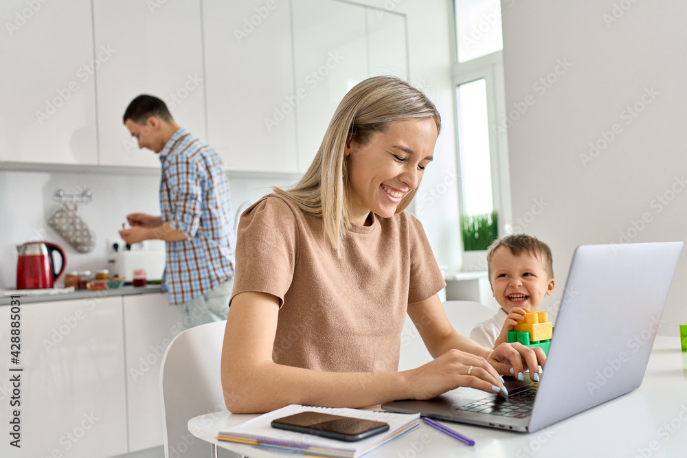 © insta_photos - Happy young mom business woman distance working online using laptop computer while small funny kid son playing having fun sit at kitchen table. Virtual homeoffice work and child care in family life. © insta_photos - Happy young mom business woman distance working online using laptop computer while small funny kid son playing having fun sit at kitchen table. Virtual homeoffice work and child care in family life.