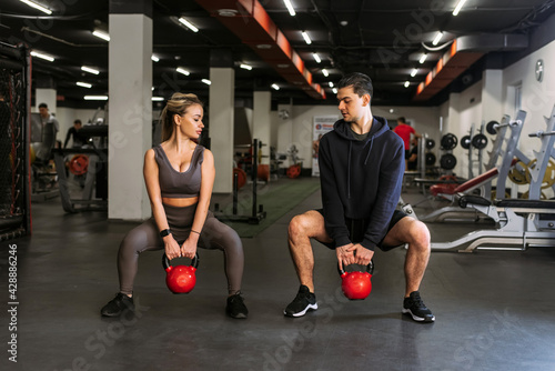 Personal trainer shows a woman how to squat with a kettlebell in a sports background