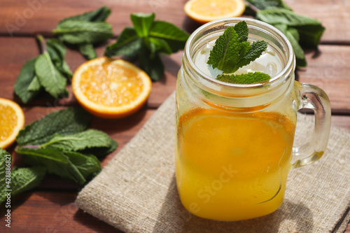 Fresh homemade citrus lemonade in a jar with oranges, mint and ice on a wooden table. Summer refreshments. Close-up, selective focus