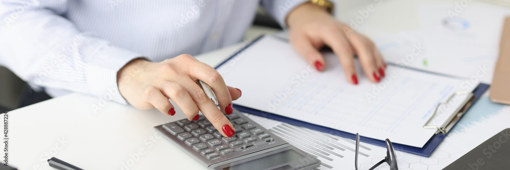 Business woman with red manicure counting on calculator in office closeup Business woman with red manicure counting on calculator in office closeup