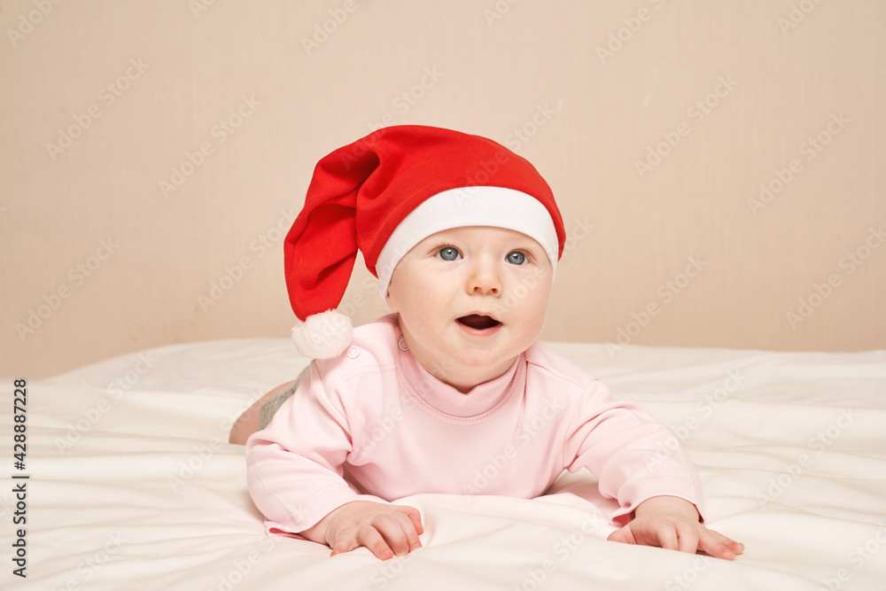 Cute small boy lying at bed. Childhood christmas concept. Light background. Smiling child. Xmas red hat. Copyspace. Stay home. Mockup. Pink female clothes Cute small boy lying at bed. Childhood christmas concept. Light background. Smiling child. Xmas red hat. Copyspace. Stay home. Mockup. Pink female clothes