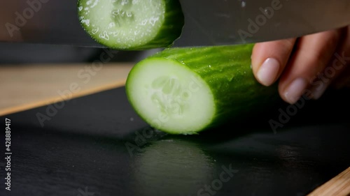 Female hands cut cucumber in round slices. Macro shot, 150 fps, slow motion. 