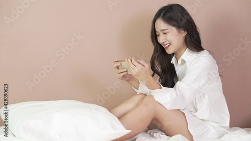 sexy woman in white shirt Laughing and touching a smartphone on bed