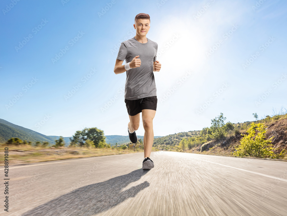 Young guy jogging on an asphalt road on a sunny day