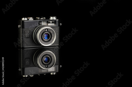 The old rangefinder automatic film camera on black glass background with reflection.