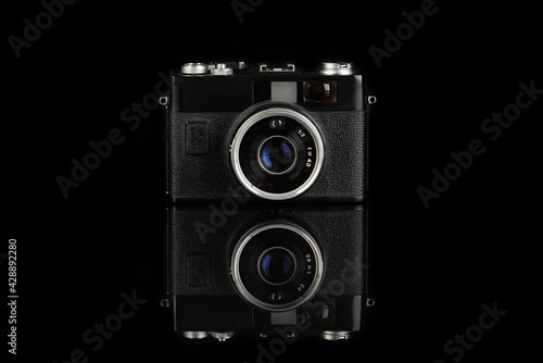 The old rangefinder automatic film camera on black glass background with reflection.